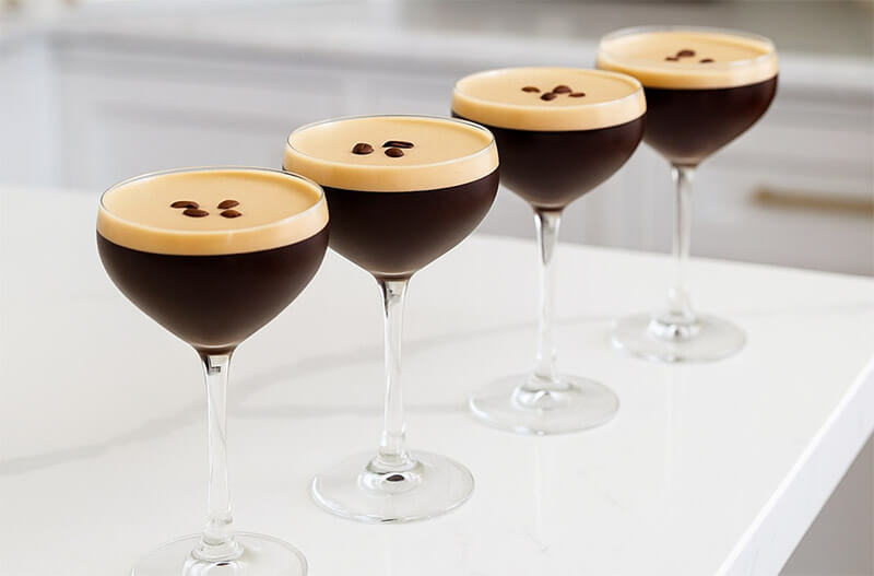Four espresso cocktails in stemmed glasses on a white surface.
