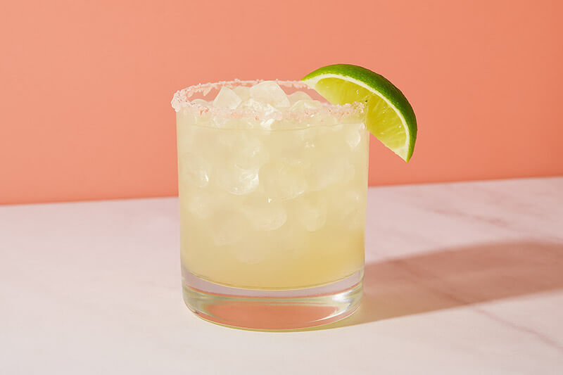 Glass of margarita with lime wedge on a peach background