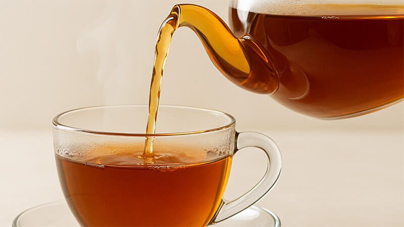 Tea being poured from a teapot into a glass cup on a light background