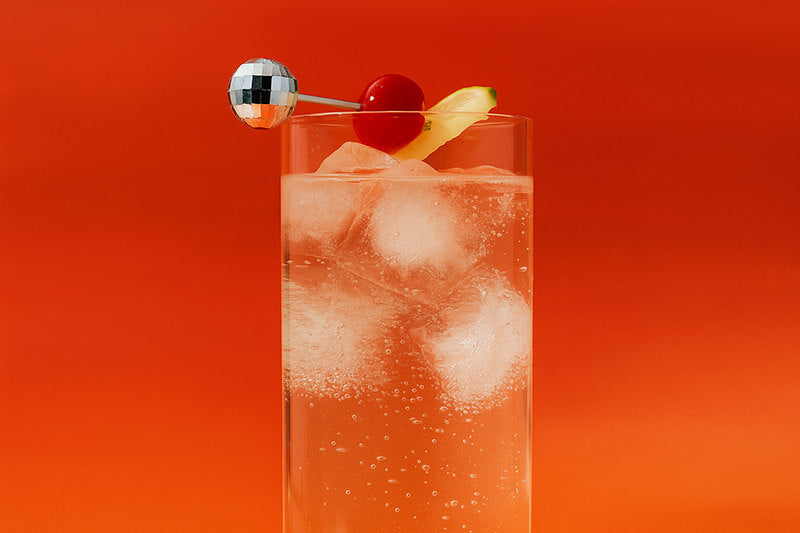 Cocktail with ice cubes, cherry, and lemon peel on a orange-red gradient background