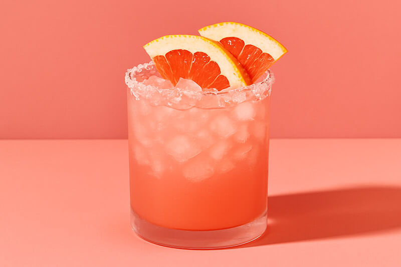 Paloma cocktail with grapefruit slices on a pink background