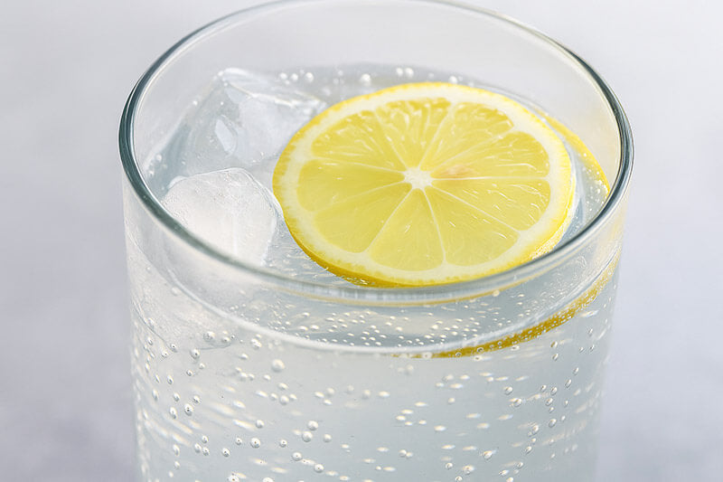 Glass of sparkling water with a lemon slice on a light gray background