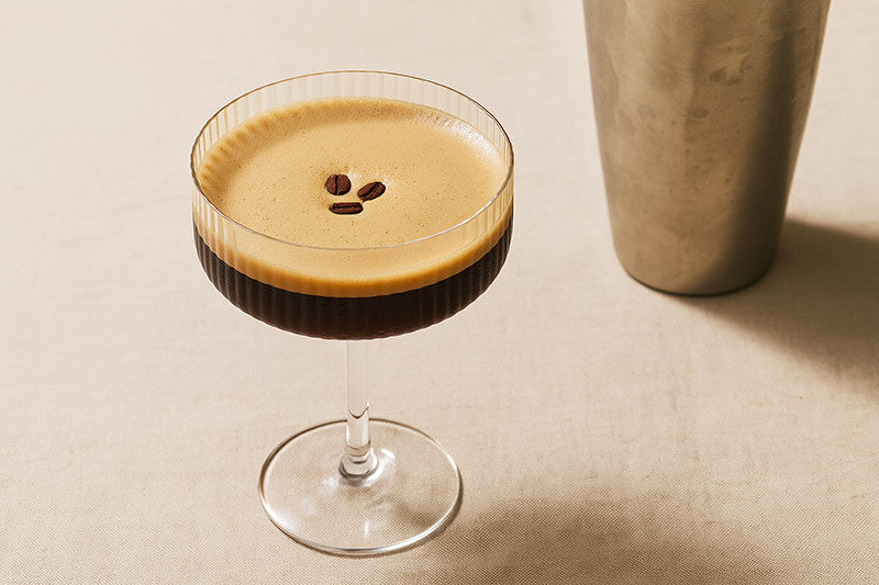 Espresso martini in a glass with a cocktail shaker on a beige background