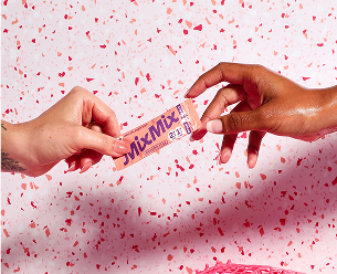 Two hands exchanging a Mixmix stick against a pink confetti background